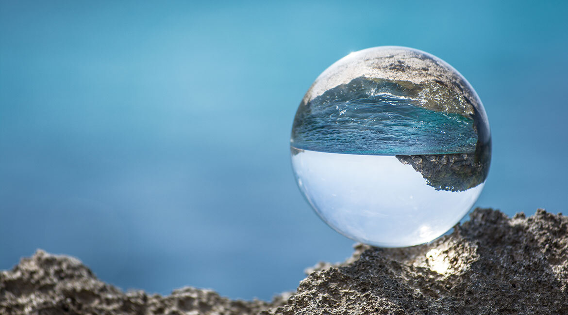 Paysage côtier inversé à travers une sphère cristalline posée sur roche.