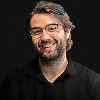 Faculty member in tech, smiling, with glasses and beard, dressed in black.