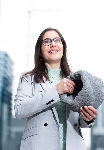 Professional in a grey coat with glasses, smiling optimistically.