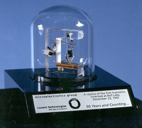 Replica of the first transistor from 1947, a pivotal invention in electronics by Bell Labs, showcased under a protective dome.