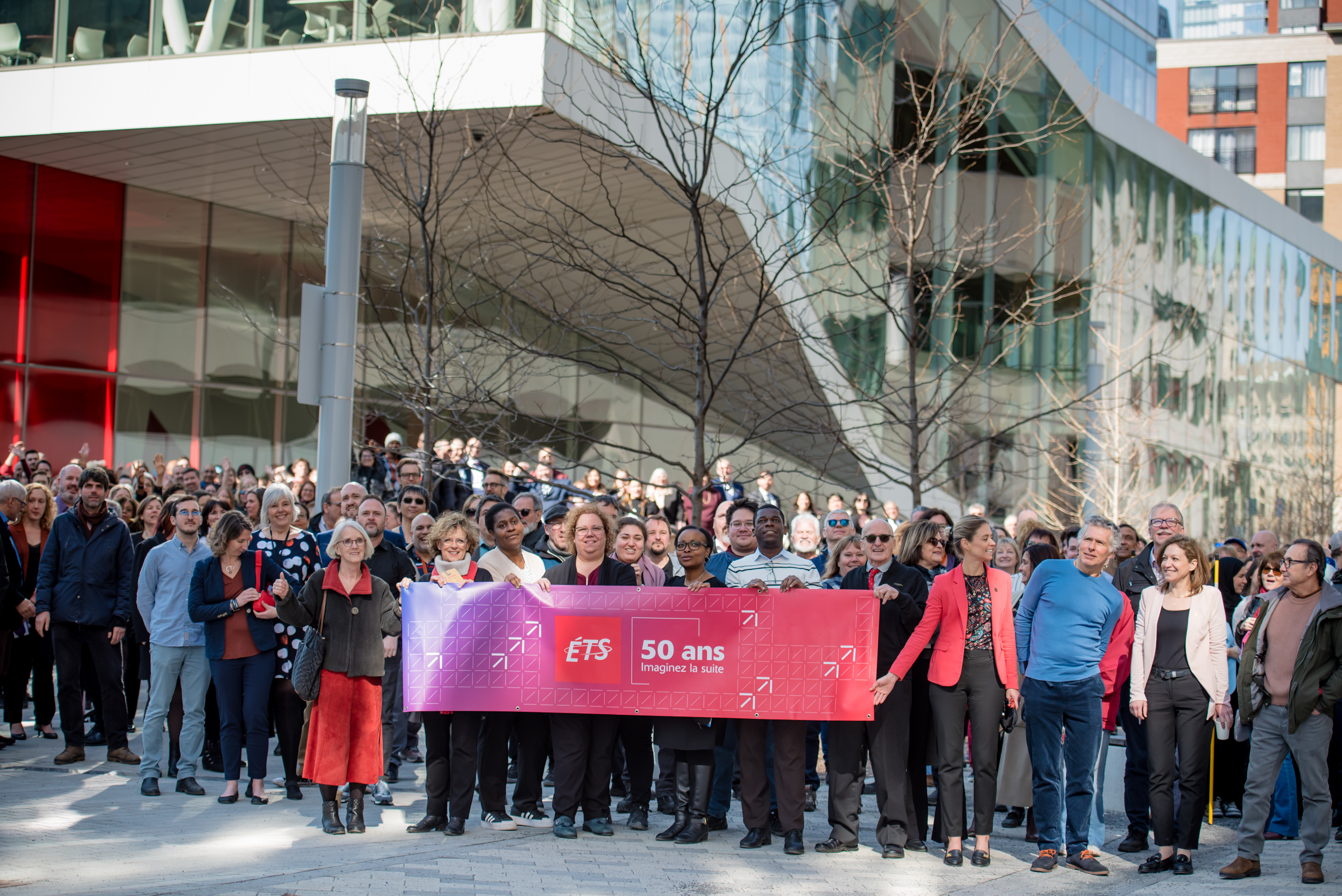 Groupe célébrant les 50 ans de l'ÉTS avec une bannière, devant un bâtiment moderne.