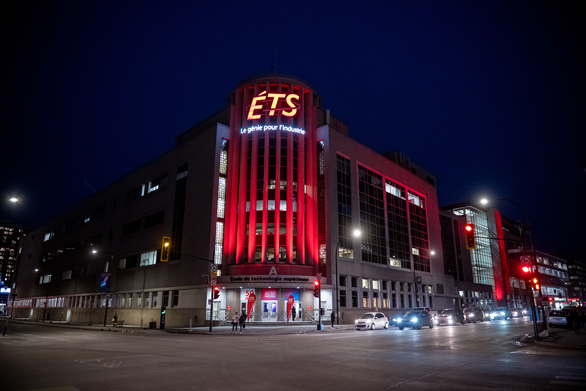 Bâtiment de l'ÉTS illuminé de nuit, symbole d'innovation et d'éducation en génie.
