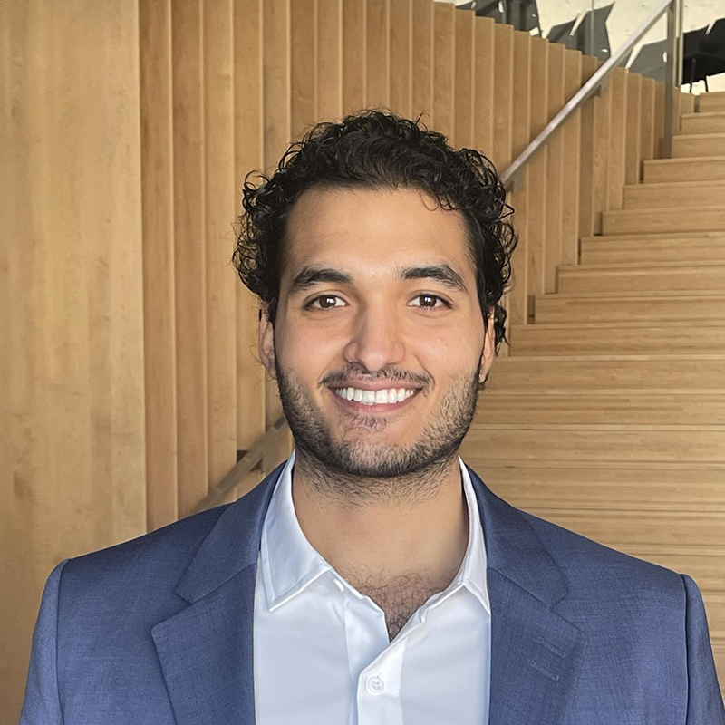 Étudiant souriant en costume, intérieur moderne avec escalier en bois.