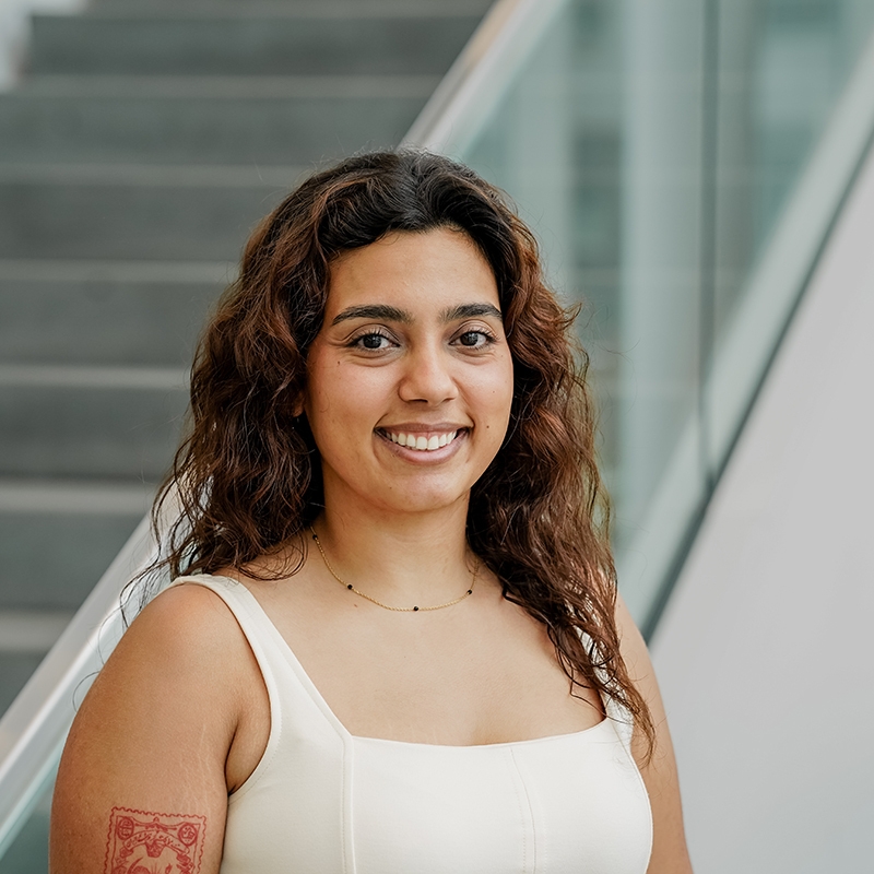 Étudiante souriante avec tatouage, en tenue décontractée, dans un cadre universitaire.