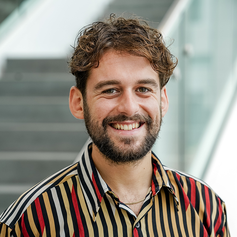 Jeune homme souriant, vêtu d'une chemise rayée, dans un cadre moderne et lumineux.