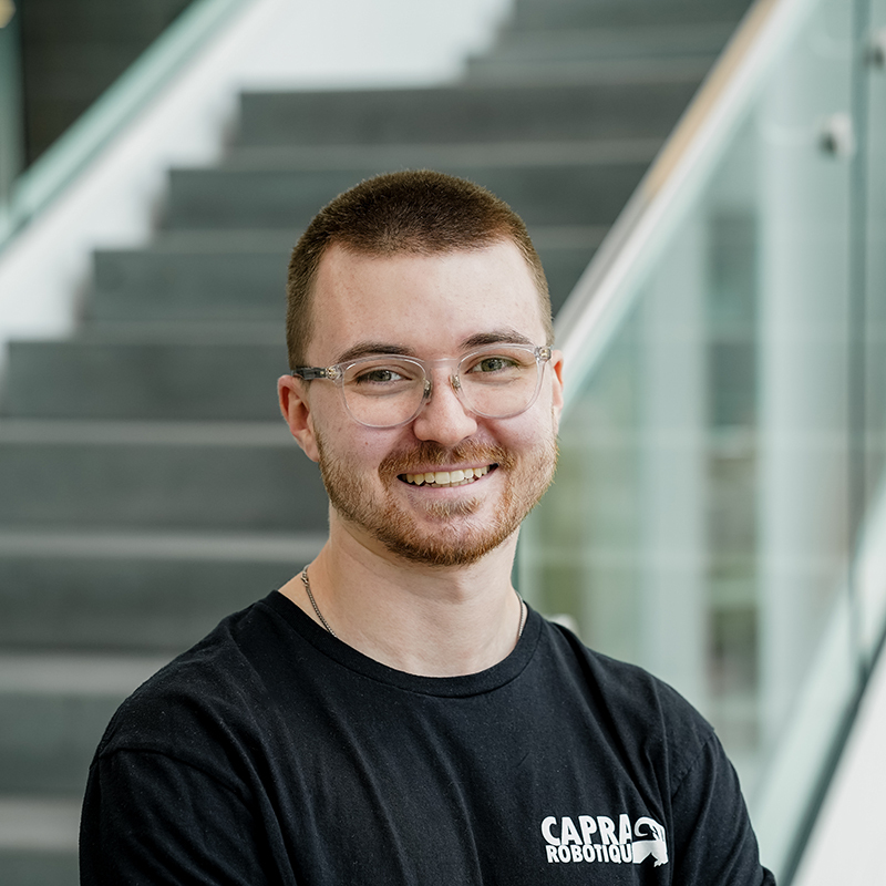 Étudiant souriant avec t-shirt de robotique, dans un bâtiment moderne.