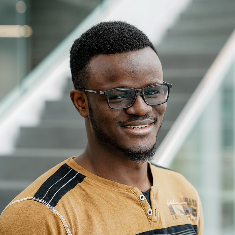 Étudiant souriant avec des lunettes devant un escalier, représentant la vie académique dynamique.