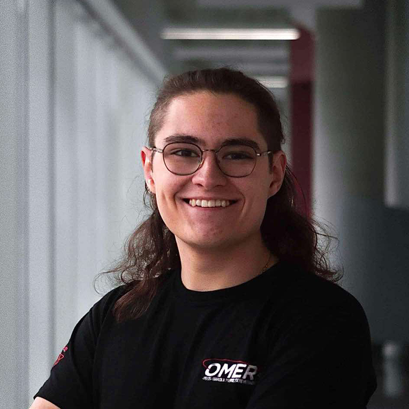 Étudiant souriant avec lunettes, vêtu d'un t-shirt d'équipe technique.