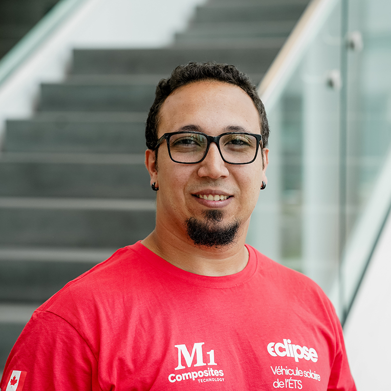 Étudiant souriant en t-shirt rouge avec logos, à l'ETS.