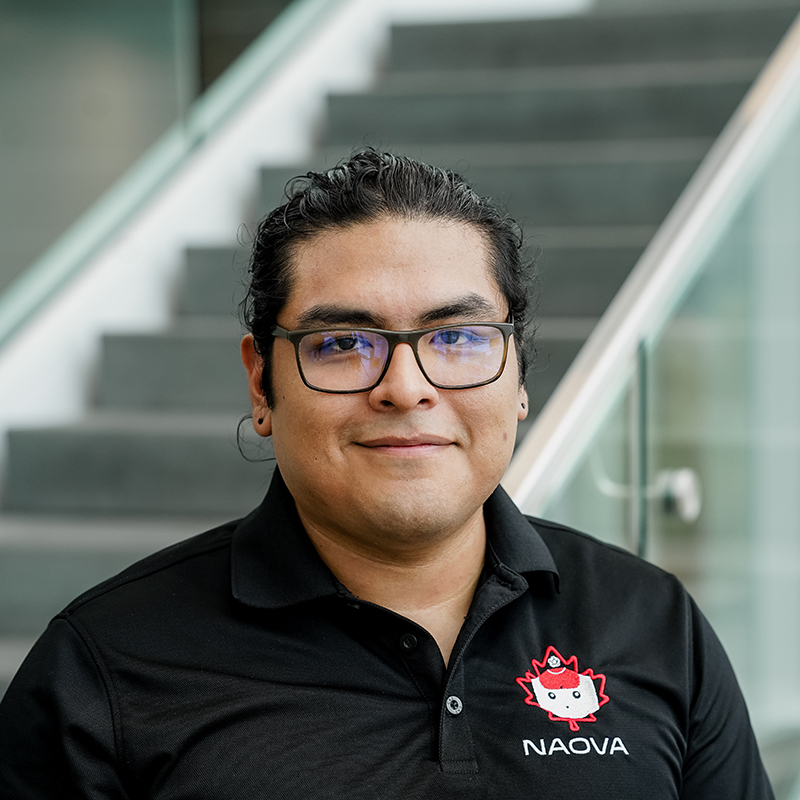 Étudiant en technologie avec un polo logo NAQVA, souriant, devant un escalier.