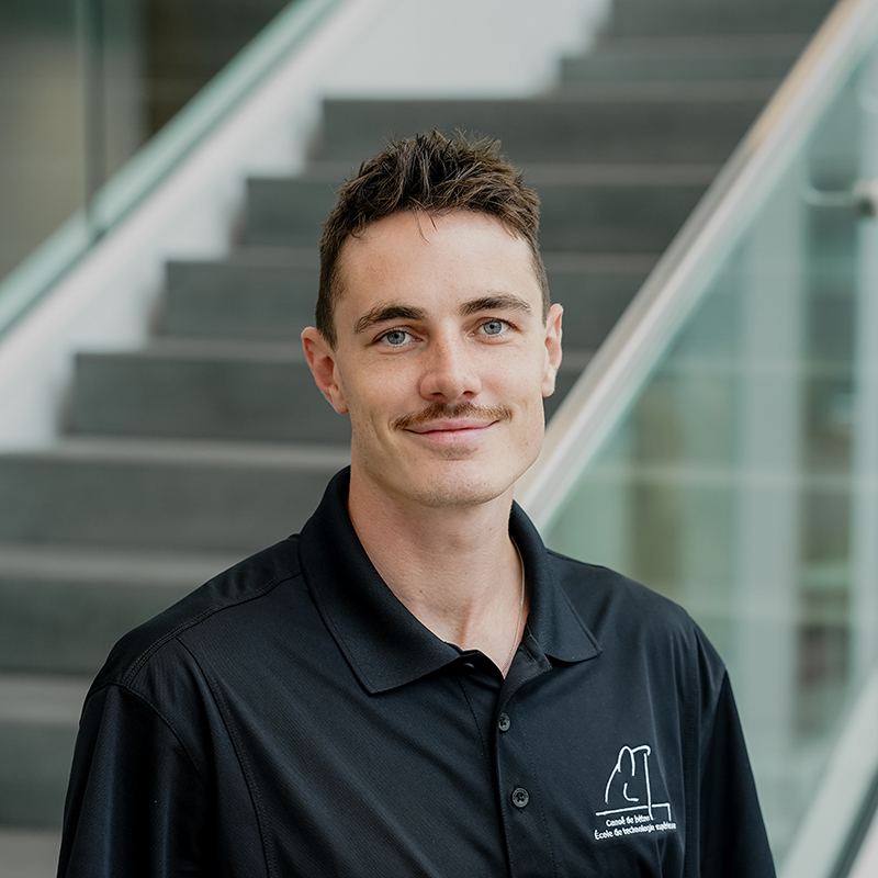 Étudiant souriant en tenue professionnelle devant un escalier, représentatif de l'avenir prometteur en technologie.