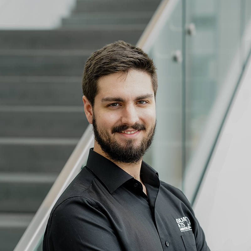 Un étudiant souriant en tenue professionnelle dans un environnement universitaire.