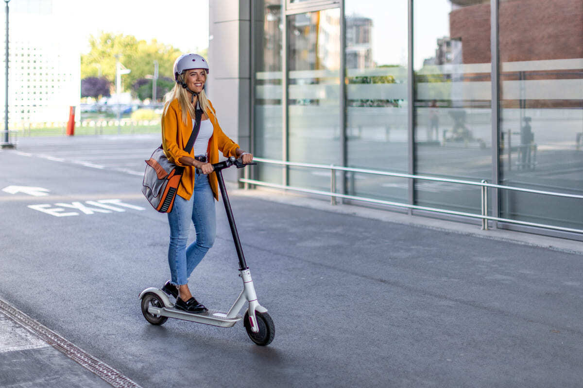Smiling student on an electric scooter at the campus. Helmet for safety.