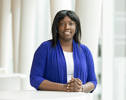 Étudiante souriante en technologie, vêtue d'un blazer bleu, symbolisant l'ambition et l'innovation académique.