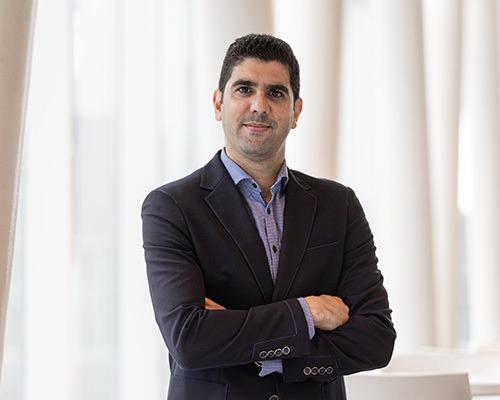 Confident professional in a suit standing with crossed arms in a modern university setting.