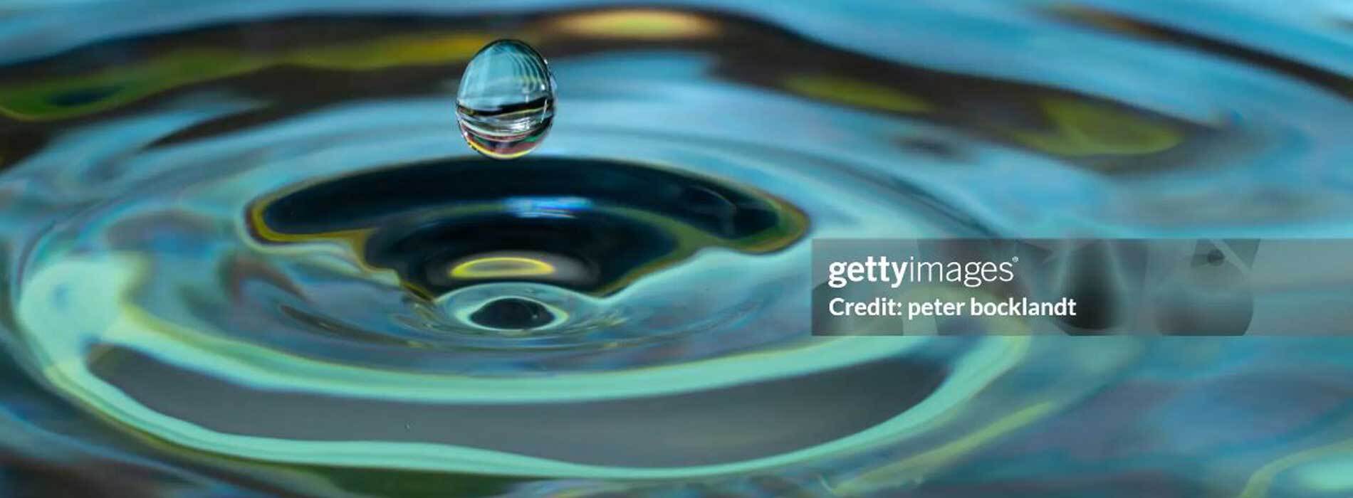 Close-up of a water droplet creating ripples on a colorful surface.