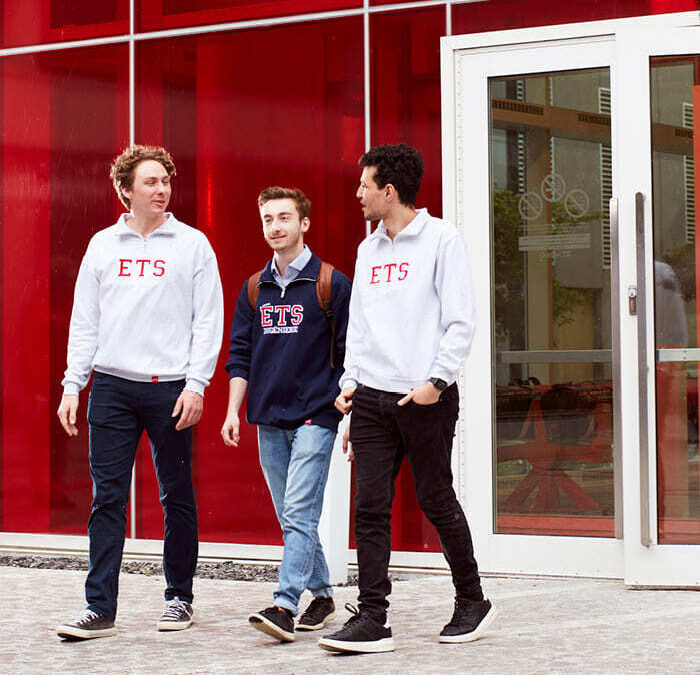 Étudiants à l'ETS marchant et discutant devant un bâtiment universitaire.