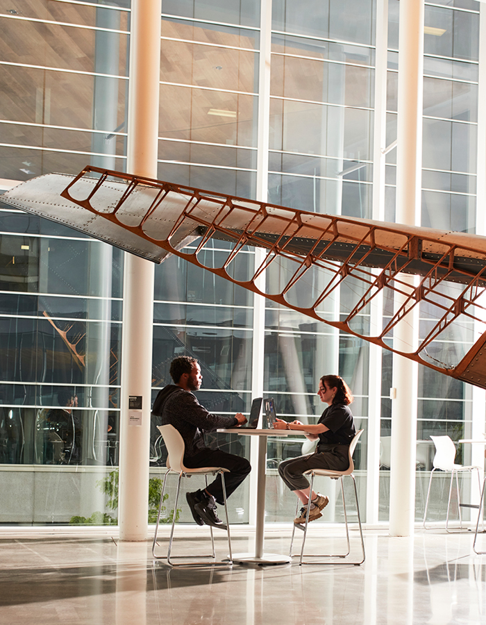 Étudiants collaborent sous une maquette d'avion, dans un atrium moderne et lumineux.