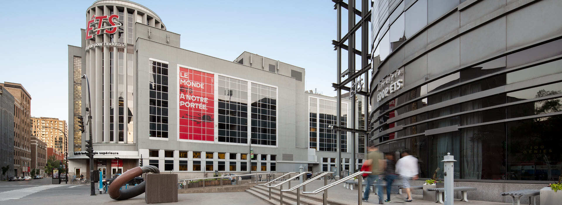 Modern university building with a large red banner, bustling with activity.