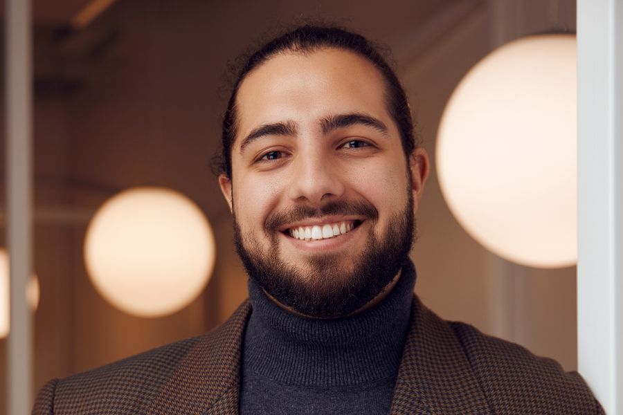 Étudiant souriant, portant un col roulé sombre et une veste à motif.