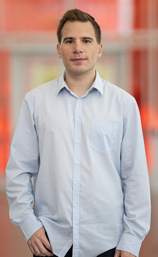 Professional in a light blue shirt with a confident stance in a modern university setting.