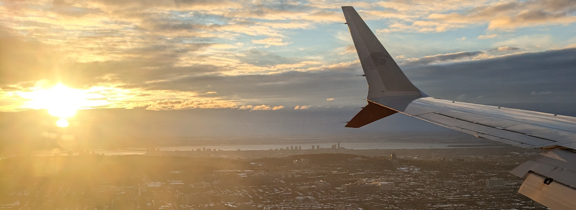 Vue aérienne au lever du soleil avec l'aile d'un avion et une silhouette urbaine.