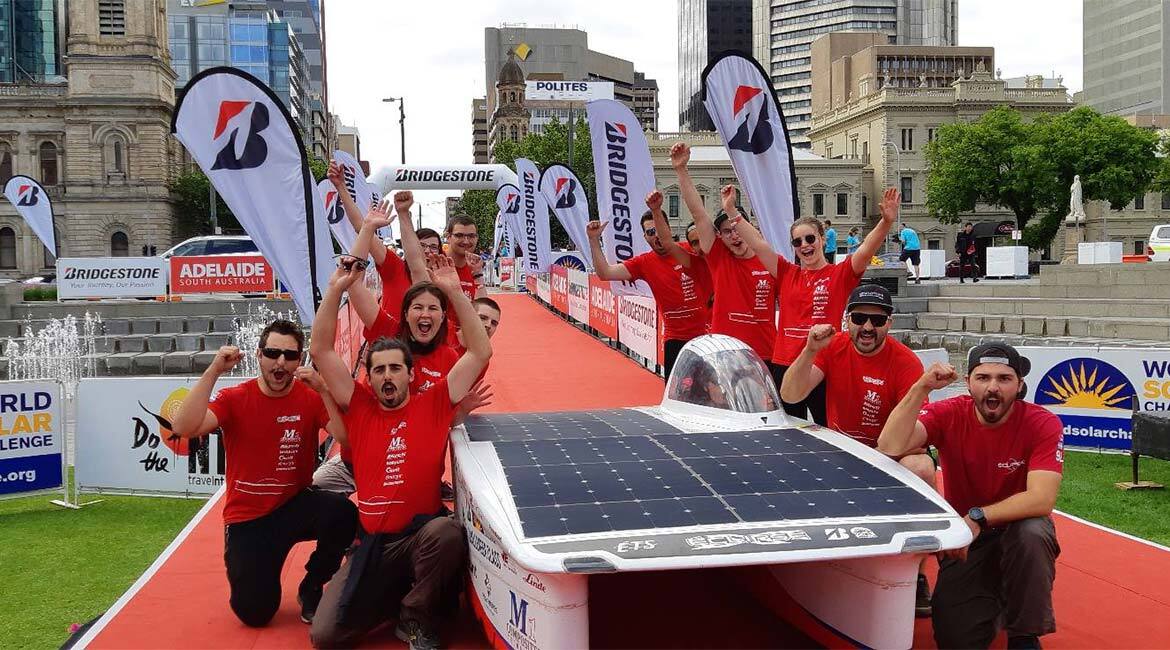 Équipe universitaire joyeuse avec véhicule solaire pour compétition d'ingénierie.