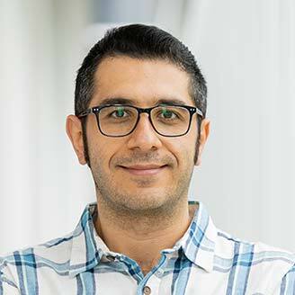 Portrait d'un enseignant en technologie, souriant, portant des lunettes et une chemise à carreaux.