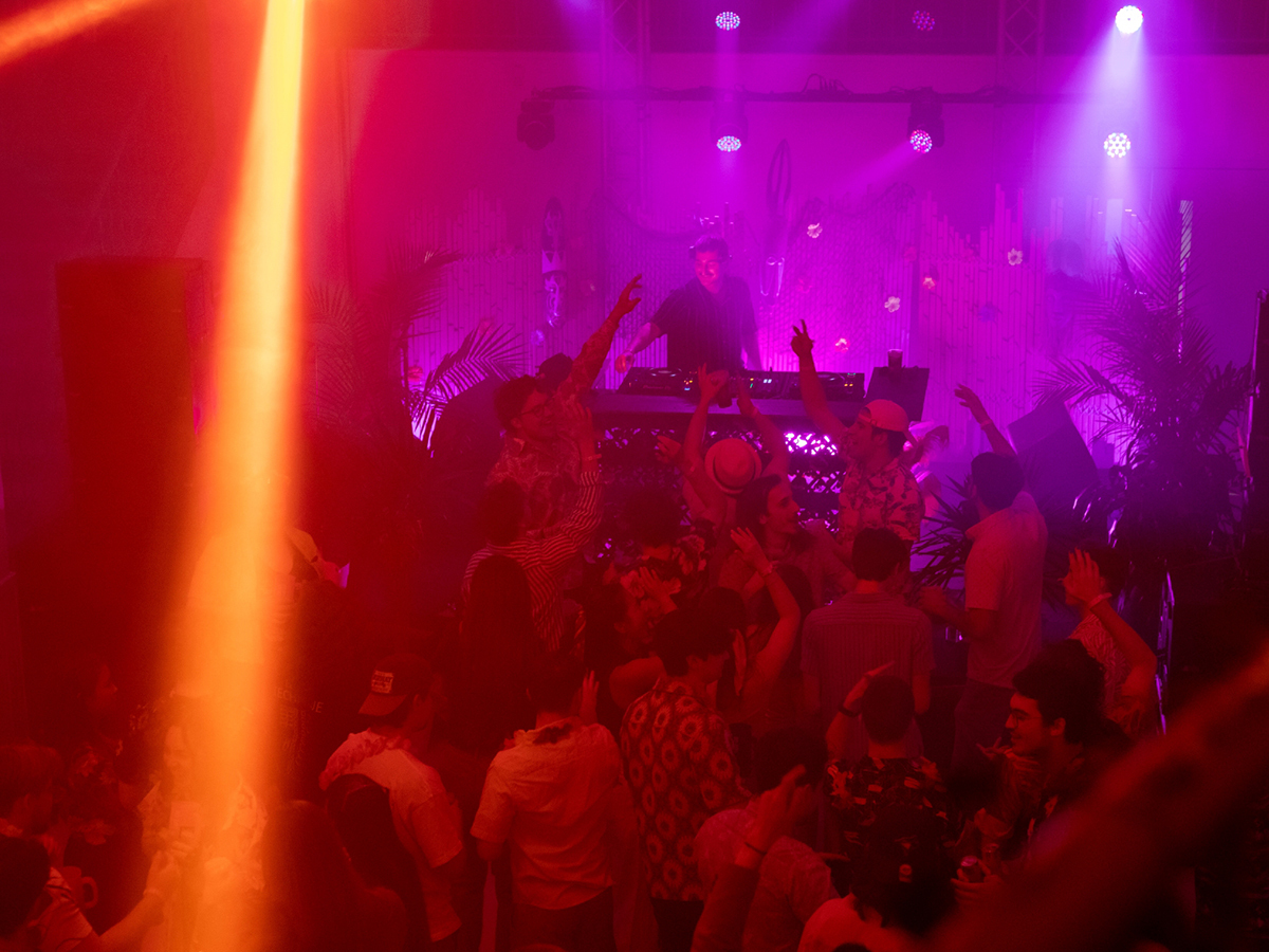 Soirée étudiante animée avec DJ et foule dansante sous des lumières vives.