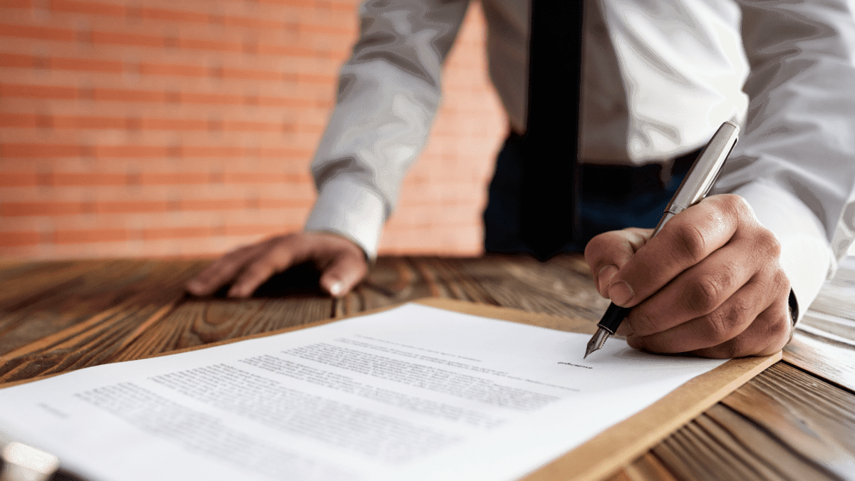 Professional signing a document at a wooden table.