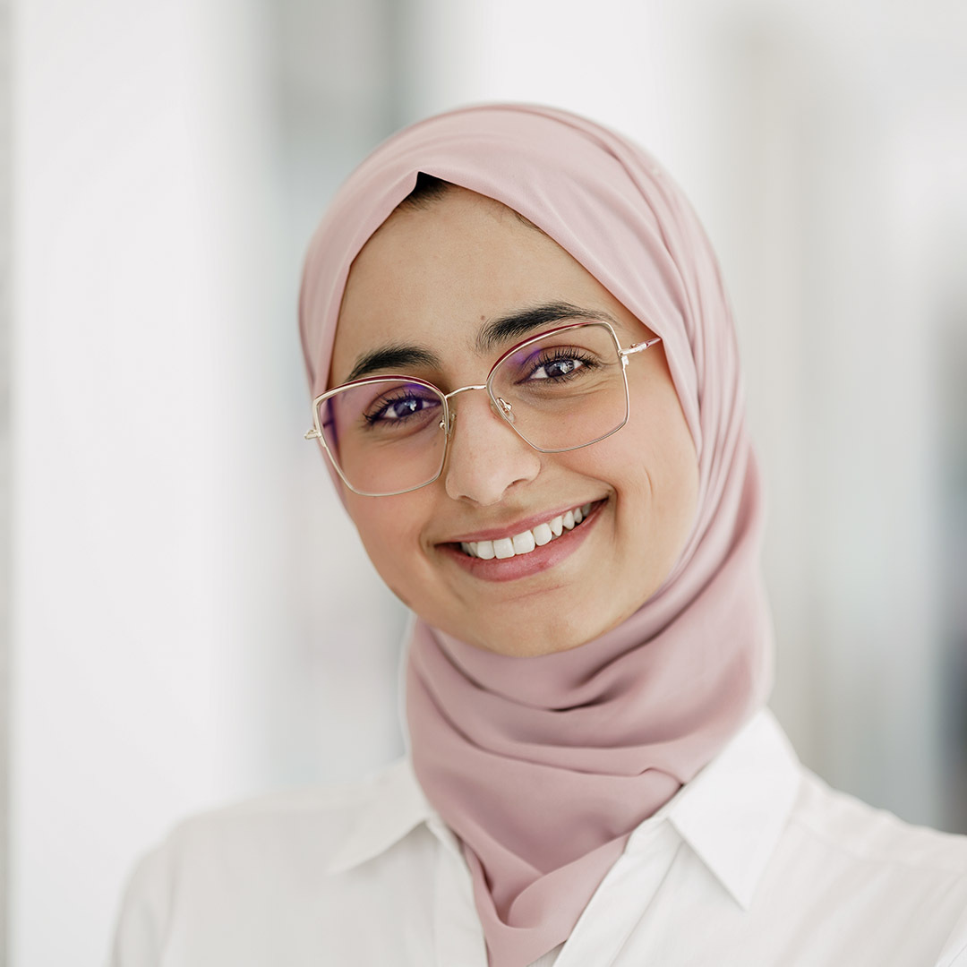 Étudiante souriante en blouse blanche et hijab rose, symbolisant la diversité et l'inclusion.