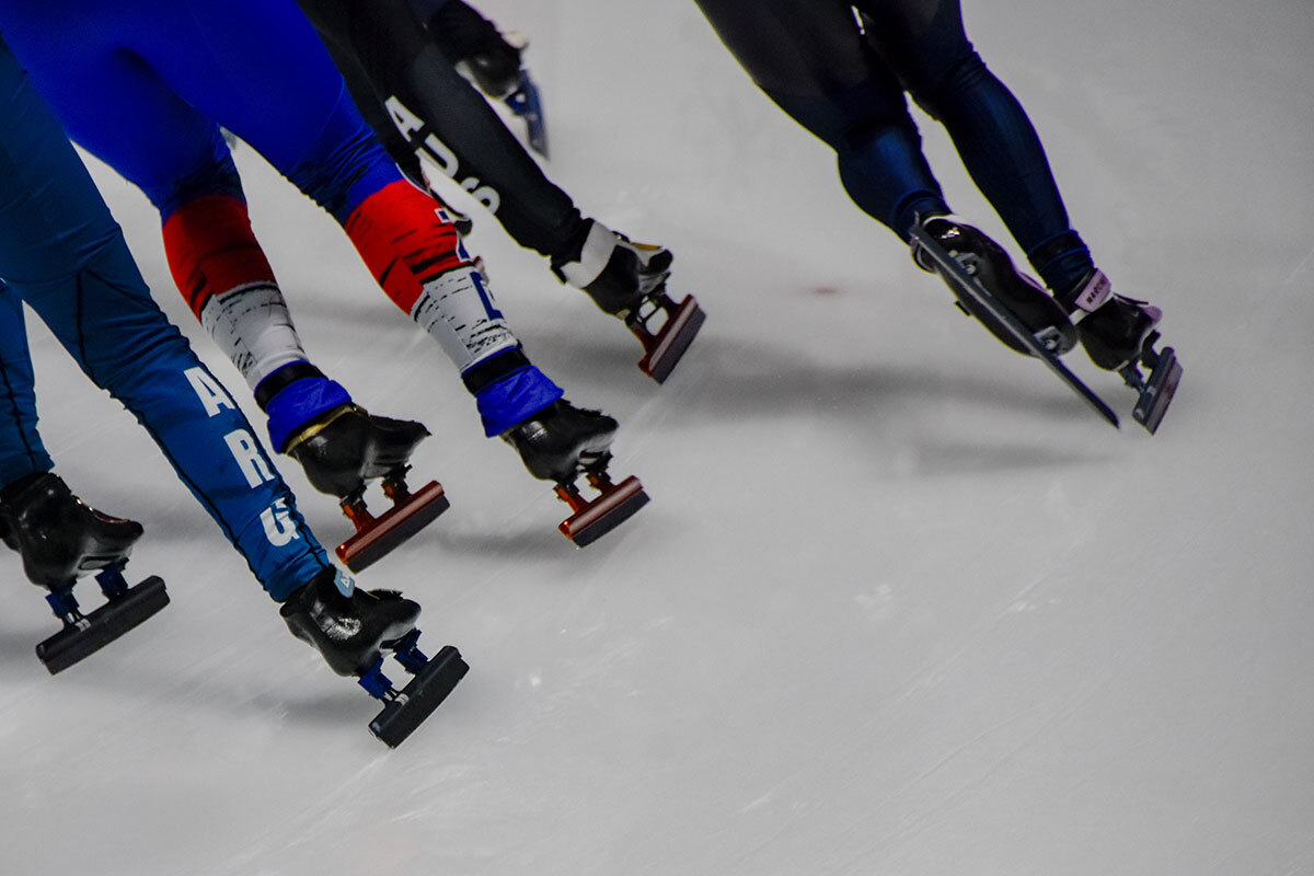 Speed skaters racing on ice with focus on skates and legs.